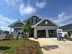 A modern gray house with white trim, a front porch, and a double garage sits under a blue sky at 76 Moon Flower Walk, Youngsville. Fresh landscaping surrounds the driveway, and a sign in front indicates the home is available.