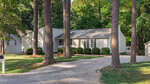 Nestled in Henderson, 165 Dorsey Place is a single-story light gray house with a metal roof, set behind tall trees and lush greenery, with a curved gravel driveway welcoming you to the front.