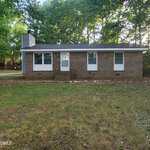 Charming single-story brick house at 443 Park Avenue, Youngsville, featuring three front windows, a central door, and a cozy front porch. Surrounded by grass and trees with a wooded area in the background.