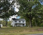 A two-story white house with black shutters sits among large trees on a grassy lawn beside 6663 Harold Obrien Road in Oxford, with a detached white garage visible in the background.