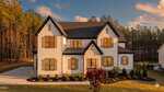Modern two-story white house with black trim and roof at 190 Cherry Bark Drive, Youngsville, featuring large windows, stone accents around the front door, a landscaped yard, and trees under a partly cloudy sunset sky.