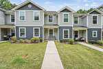 Located in Franklinton, 918 E Green Street Unit G107 is a two-story townhouse with gray siding, white trim, and a covered entryway. Trimmed bushes and a green lawn border the walkway to the front door, with neighboring units on both sides.