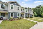 A row of modern two-story townhouses in Franklinton with gray siding, white trim, and small landscaped front yards lines 918 E Green Street Unit G107, set along a curved sidewalk with trees and greenery in the background.