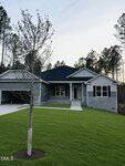 A modern single-story gray house with white trim at 30 Watermelon Drive, Franklinton, features a covered front porch and attached garage. It sits on a bright green lawn with a young tree in the center, framed by tall pine trees in the background.