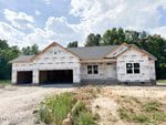 A single-story house under construction at 55 Kettle Creek Drive, Zebulon, features exposed walls covered in white weatherproof sheathing, an unfinished driveway, and a three-car garage, set against trees and a partly cloudy sky.