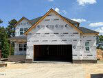 A two-story house under construction at 10 Diamond Creek Drive in Zebulon, with exposed framing and home wrap. The garage door is open, the roof nearly finished, and trees frame the scene beneath a clear blue sky.