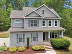 Two-story gray house with white trim, front porch, and black door at 3689 Summer Springs Drive in Franklinton. Well-maintained landscaping features bushes, mulch, a tall shrub by the entrance, plus a driveway on the left surrounded by trees.