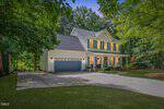 A two-story house with light blue siding, white trim, a covered front porch, and a two-car garage at 25 Ballinger Drive in Youngsville. The home is surrounded by green trees and a well-maintained lawn on a sunny day.