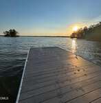 A wooden dock at 317 Doc Lane extends over a calm Manson lake at sunset, with golden reflections on the water; trees line the shore and a small island is visible in the distance.