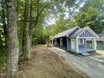 A small, dark blue house with white trim sits next to a dirt and gravel driveway at 217 Lanier Street in Oxford, surrounded by tall green trees and a partially cleared yard on a sunny day.
