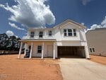 A newly constructed two-story white house at 5 Heartleaf Square, Youngsville, features a covered driveway and garage on a bare red dirt lot beneath a partly cloudy sky, with trees lining the background to the left.