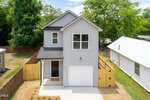 Charming two-story gray house at 210 Orange Street, Oxford features a single-car garage, black roof, and white trim. A wooden fence encloses the backyard, while the front yard boasts a small lawn and young plants.