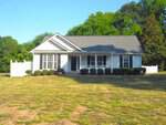 Charming single-story white house at 3582 Copper Creek Lane, Franklinton, with a gray roof, front porch and white railing. Features large front windows, small shrubs along the front, and a spacious, slightly dry lawn with trees behind.