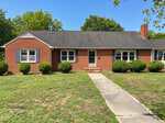 Charming single-story red brick house at 309 Broad Street, Oxford, with black shingle roof, white trim, two front windows with dark shutters, a right-side chimney, trimmed shrubs, and a concrete walkway to the entrance.
