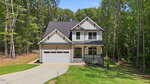 Two-story modern farmhouse at 627 Shawnee Drive in Louisburg features white siding, dark trim, a gable roof, covered front porch, and two-car garage, all nestled among trees and a well-kept lawn on a sunny day.