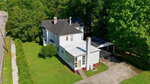 Aerial view of a two-story white house with a black roof, sunroom, and carport at 845 S William Street in Henderson, surrounded by green trees and grass, next to a sidewalk and road.