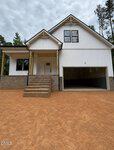 A modern two-story house at 148 Mohawk Drive in Louisburg features white siding, a covered front porch, brick steps and foundation, black trim, and a two-car garage, set on a dirt driveway with trees in the background.