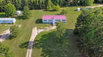 Aerial view of a single-story house with a red roof at 150 Freedom Lane, Henderson. Front steps lead to a large grassy yard bordered by trees, and a gravel driveway curves from the lower edge toward the house, with other small structures nearby.
