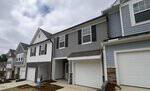 A row of modern townhouses on 224 Alberta Drive in Franklinton features gray, white, and blue siding, stone accents, and white garage doors under a cloudy sky. Mulched landscaping lines the driveways in front of the homes.