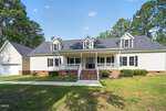 Located at 161 Sequoia Drive in Louisburg, this large two-story house features cream siding, black shutters, three dormer windows, a spacious front porch with white railings, brick steps, an attached garage, and a scenic lawn surrounded by trees.