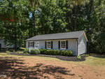 A small, single-story house with light gray siding, black shutters, and a dark roof sits surrounded by trees at 939 Cheves Road in Zebulon, featuring a well-kept front yard and tidy landscaping along the front.