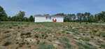 A small white house with a red roof and front steps sits alone on a large, dry, patchy grass field at 70 Waterfront Drive, Louisburg, surrounded by trees under a clear blue sky.