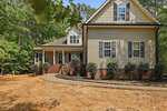 A beige two-story house with black shutters and a brick foundation sits at 2130 Turquoise Lane in Franklinton. Surrounded by shrubbery, trees, and bordered by woods, it features a curved walkway to a covered front porch and patchy grass in the yard.