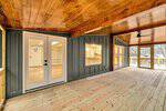 Spacious covered porch at 950 Cedar Cove Road, Henderson, with wood flooring and ceiling, dark paneled wall, large windows, and double glass doors opening to a bright interior; outdoor area visible in the background.