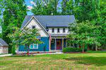A two-story house on 262 Youngsville Boulevard S with blue and white siding, a covered porch with red door, well-kept yard, and trees in the background on a bright, sunny day in Youngsville.