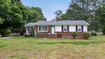 A single-story brick house with white siding at 5508 Forest View Heights, Oxford, features a small front porch with steps, a few bushes in front, trees in the background, and a carport on the left side of the yard.