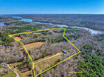 Aerial view of a large wooded and partially cleared property at 560 Little Rosewood Lane, outlined in yellow, surrounded by forest and near a lake in Henderson. Some buildings and dirt roads are visible within and around the outlined land.