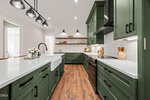 Modern kitchen at 400 Pilot Ridge Road in Zebulon with green cabinets, white countertops, farmhouse sink, stainless steel appliances, white subway tile backsplash, wood floors, and open shelves with decor, under black pendant and wall lighting.