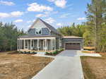 A modern gray house with a large porch, white trim, and a two-car garage sits on a spacious lot with trees in the background and a concrete driveway leading to the front entrance.