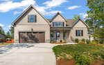 A modern suburban house at 350 Pilot Ridge Road in Zebulon, with beige siding, stone accents, and a large brown garage door, set on a wide driveway and surrounded by landscaped lawn and trees under a blue sky.