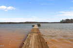 A wooden dock extends out over a large lake at 98 Shady Lane in Henderson, with calm water and a distant tree-lined shoreline under a blue sky with scattered clouds.