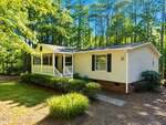 A single-story beige house at 224 Grandpa Way, Spring Hope, features a covered front porch with white railings and dark shutters, surrounded by green trees and bushes under a clear blue sky.