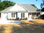 Charming single-story home at 300 S Elm Street in Creedmoor featuring gray siding, white trim, a two-car garage, large windows, covered entry with wooden columns, and a landscaped front yard with shrubs and mulch.