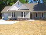 A newly built single-story house at 306 S Elm Street in Creedmoor features gray siding, stone accents, large windows, and a covered porch. Enjoy fresh landscaping with straw ground cover and a driveway leading to a single-car garage.