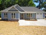 Charming single-story blue house with white trim in Creedmoor at 308 S Elm Street. Features a covered front porch, attached single-car garage, multiple front windows, freshly mulched yard, concrete driveway and walkway, and trees in the background.