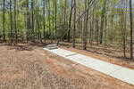 A concrete pad with a picnic table and benches sits in a clearing surrounded by tall trees at 101 Nebow Lane, Louisburg; bricks line the edge and a wooden beam rests on the ground.