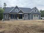 A modern, single-story house at 440 Pilot Ridge Road, Zebulon, features blue-gray siding, stone accents, white trim, a covered porch, gabled roof, and large windows, set on a dirt yard with trees in the background.
