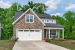 A modern suburban house at 35 Deacon Ridge Lane, Youngsville, with a stone facade, two-car garage, and covered front porch, surrounded by green trees and bushes on a sunny day.