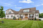 A large, modern farmhouse-style home at 15 Old Garden Lane in Youngsville, with white siding, a dark roof, and stone steps leading to a covered front porch. The yard is well-manicured with green grass, shrubs, and a small tree in front.