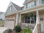 A two-story suburban house in Wake Forest with stone and siding exterior, double garage, covered front porch with white railing, potted plants, hanging ferns, and house number 2525 displayed by the door.