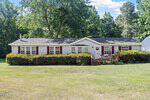 A single-story house with white siding, red shutters, and a small front porch sits at 4122 Old Franklinton Road. Surrounded by green bushes, trees, and a large grassy yard, the home backs up to a wooded area in peaceful Franklinton.