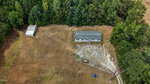 Aerial view of a single-story house with a gray roof at 190 Upchurch Road, Zebulon, near dense trees, featuring a detached shed on a large, mostly cleared grassy plot bordered by woods.