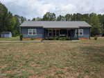 A single-story blue house at 4519 J I Oakes Road in Bullock features a covered front porch, sits on a large dry lawn with shrubs and trees, and includes a small white shed to the left. The sky is partly cloudy.