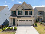 Two-story beige house with green shutters and a two-car garage, located in a suburban Wake Forest neighborhood. A concrete driveway leads to the garage at 228 Hopewell Lane, with small shrubs and mulch in the front yard.