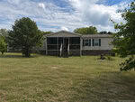 A single-story house in Castalia with a covered front porch, steps leading to the entrance, and several windows. The grassy, spacious yard at 6532 NC 56 E features a few trees under a partly cloudy sky.