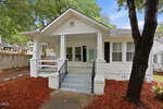 Charming white single-story home at 305 Gilliam Street, Oxford, with a covered front porch, columns, black shutters, and a blue door. Enjoy landscaped yards with red mulch, trees, and a wooden fence on the left side.